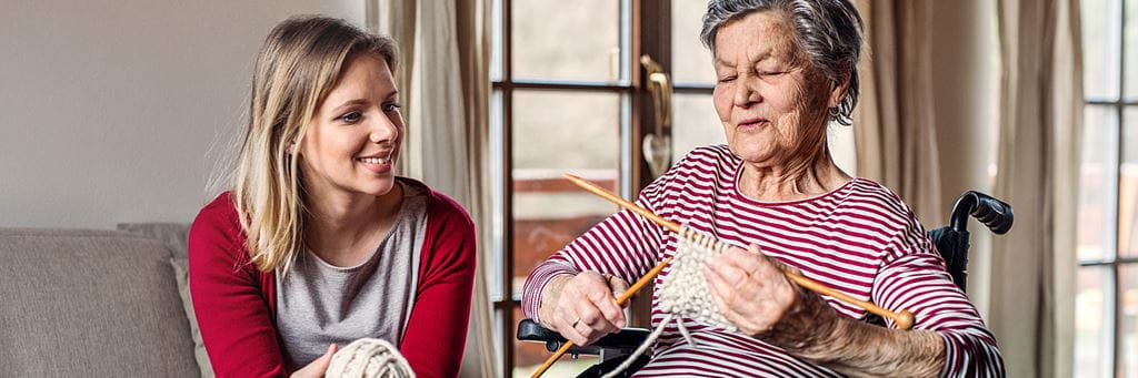 A grandmother and granddaughter knit together.