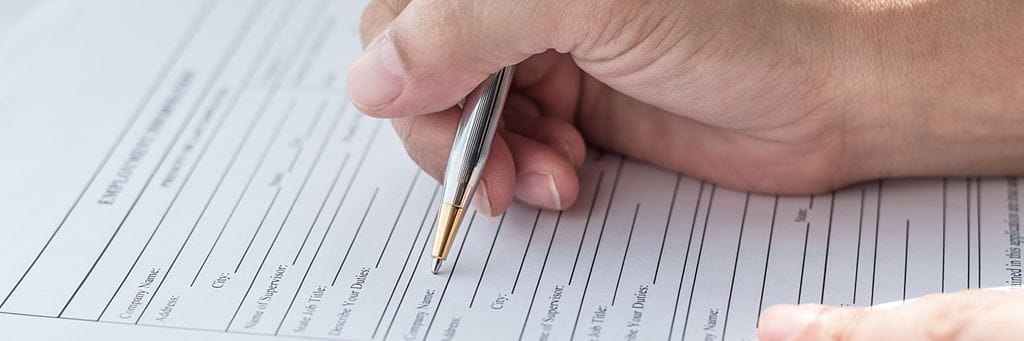 A person filling out whole life insurance forms with a pen.