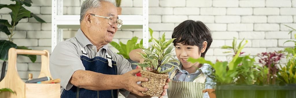 A retired grandfather teaches his grandson about gardening while holding potted plants.