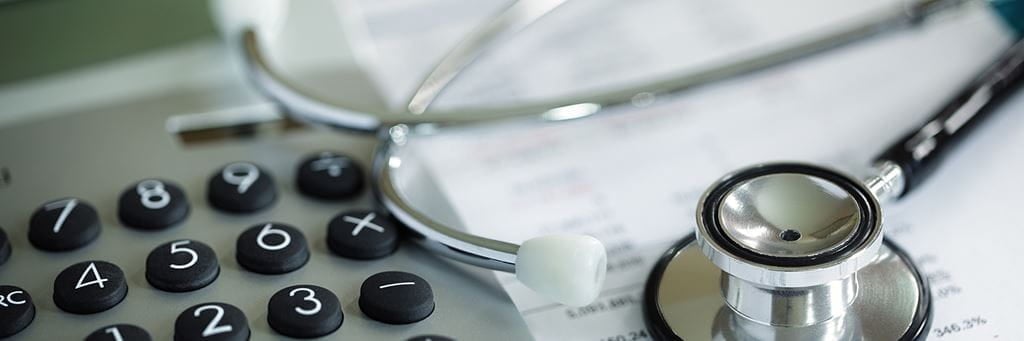 A calculator and stethoscope sit on top of health care insurance forms.