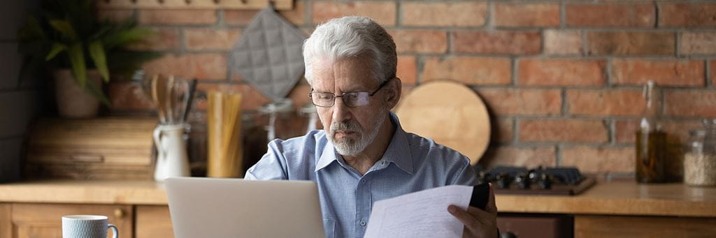 An adult man with a laptop and papers in a home office.