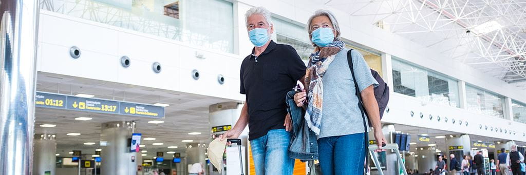 A senior couple walks through an airport terminal while wearing face masks.
