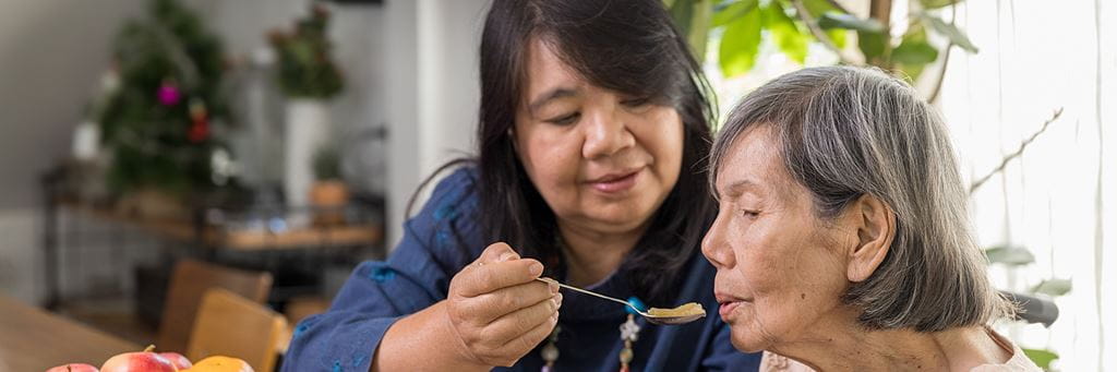 A caregiver feeding an elderly person with a spoon.