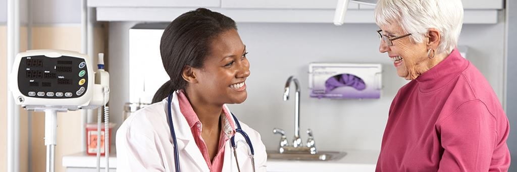A doctor speaks with a senior patient in an exam room.