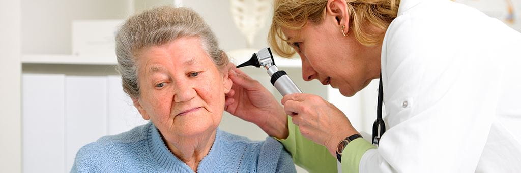 A doctor looks into a senior patient's ear during a hearing exam.