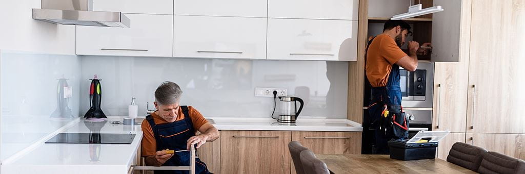Two workers install age-friendly home improvements in a kitchen.