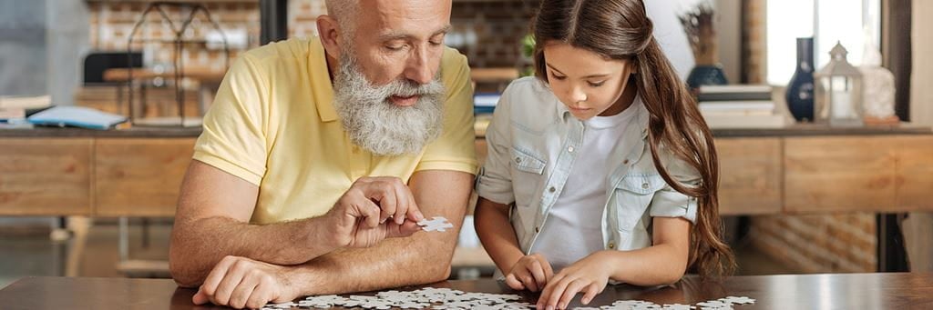 A grandfather puts together a jigsaw puzzle with his granddaughter.