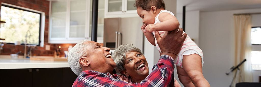 A senior couple laughing while playing with their grandchild.