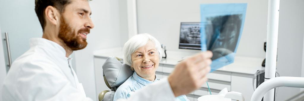 A dentist holds up an X-ray while talking to a senior patient.