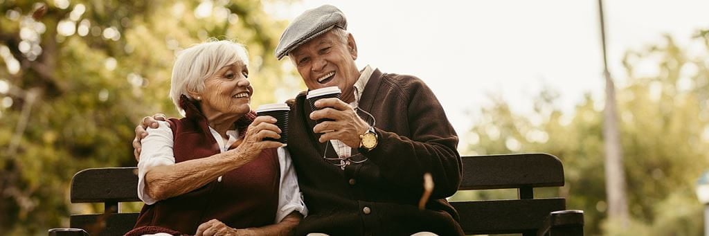 Man and woman enjoying coffee on a bench.