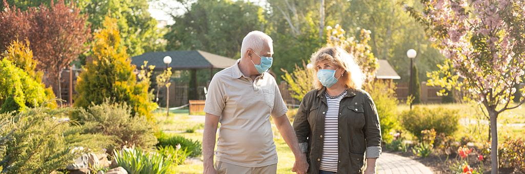 A senior couple walks outside while wearing face masks.