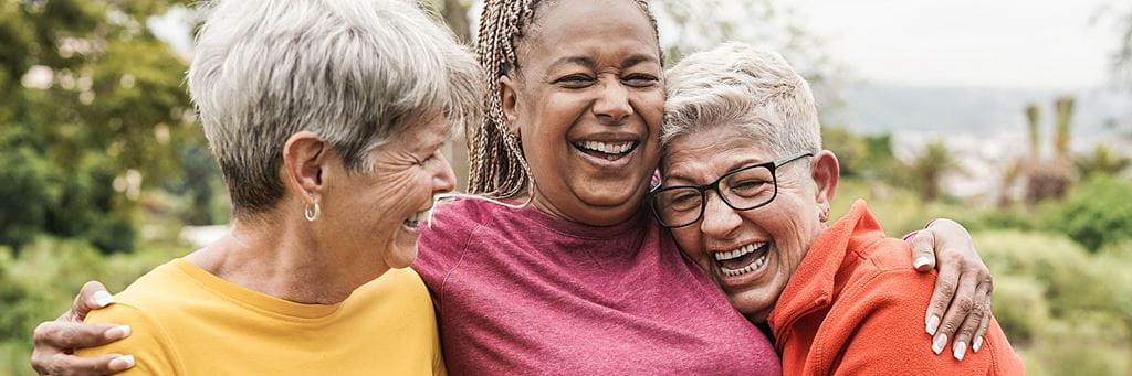 A group of three senior friends laugh together on a walk outside.