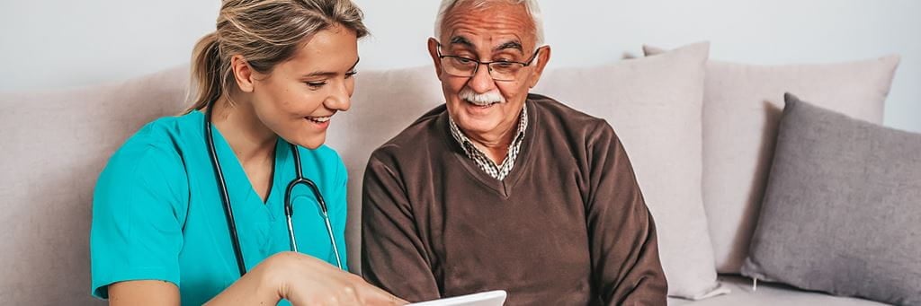 An elder care consultant shows her senior patient something on a tablet.