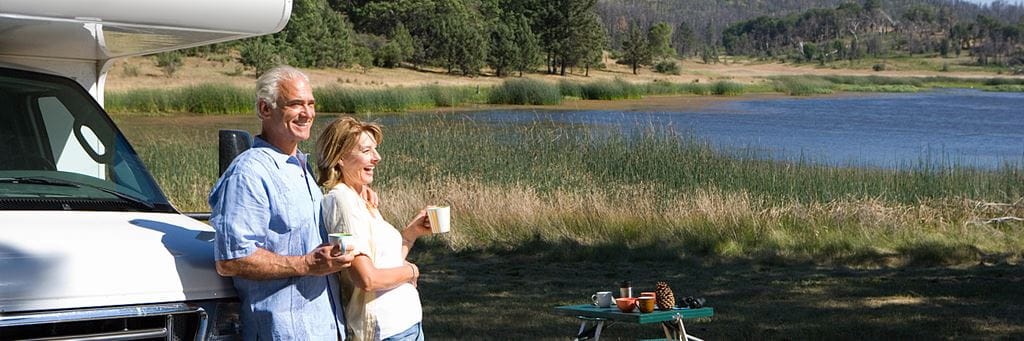 A couple enjoys coffee and a scenic lakeside view while camping with their RV.