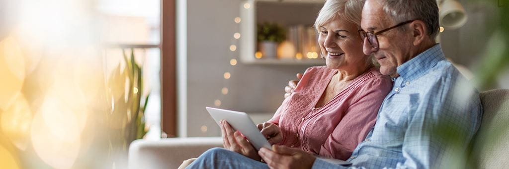 A senior couple looks up the new 2022 HSA contribution limits on a tablet in their living room.