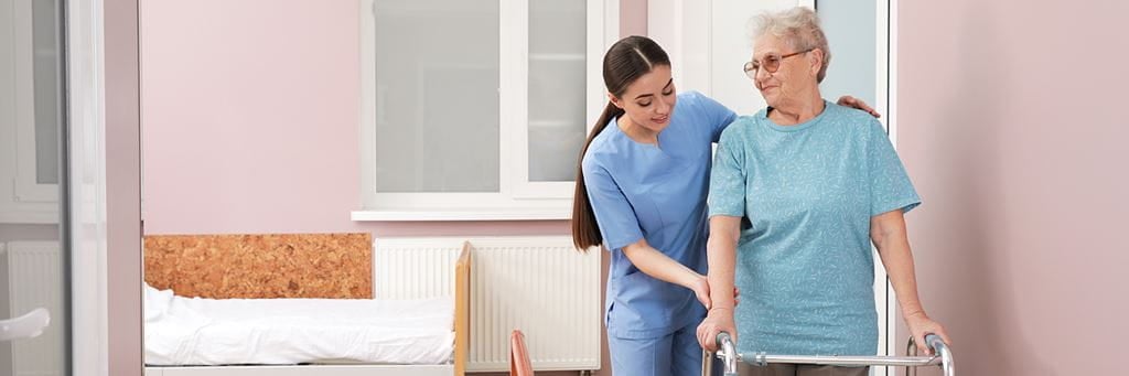 A long-term care nurse assists a senior with a walker.