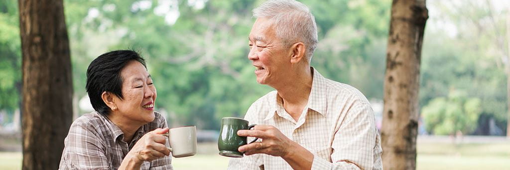 An older couple drinking coffee outside and smiling at each other.