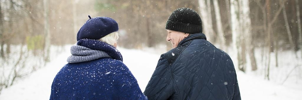 An older couple wearing warm clothing walks outside in the snow.
