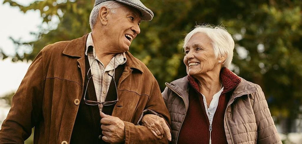 A smiling white-haired couple in winter coats enjoys a winter walk.