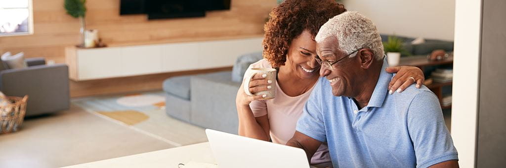 A retired couple laughs while managing their finances on a laptop.