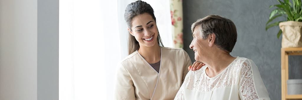 A senior woman and a caregiver smiling.