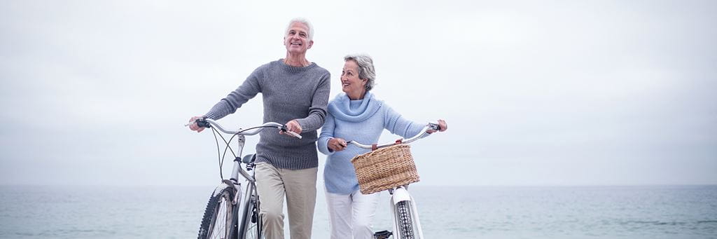 A happy retired couple rides bicycles along a paved path in a park.