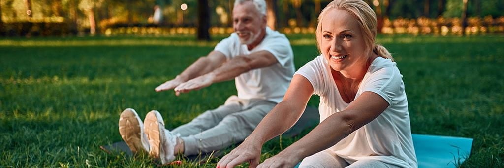 A senior couple stretches in a park.