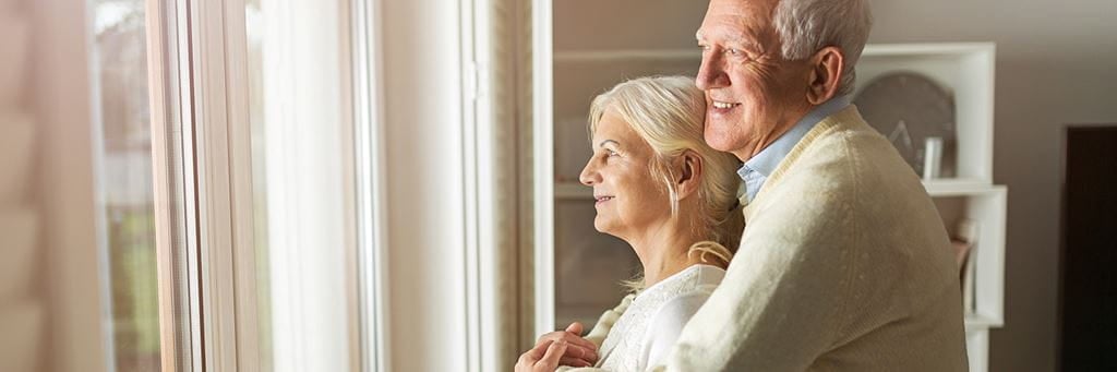 A senior couple looks out the window in their new low-income housing.