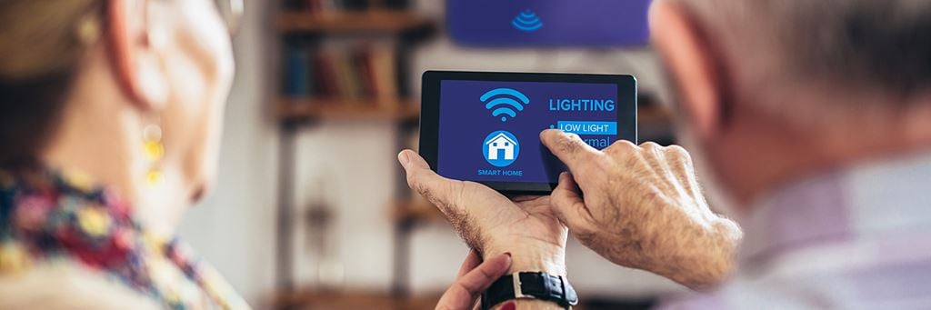 A senior couple uses a smart device to adjust the lighting in their home.