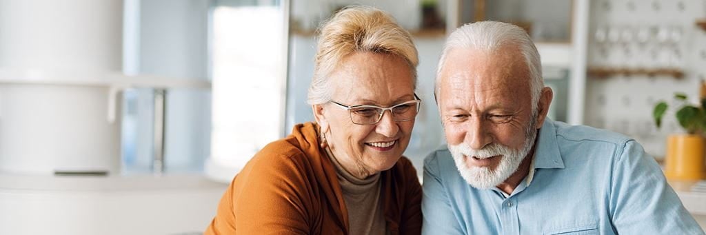 A senior couple smiles while looking at a laptop.