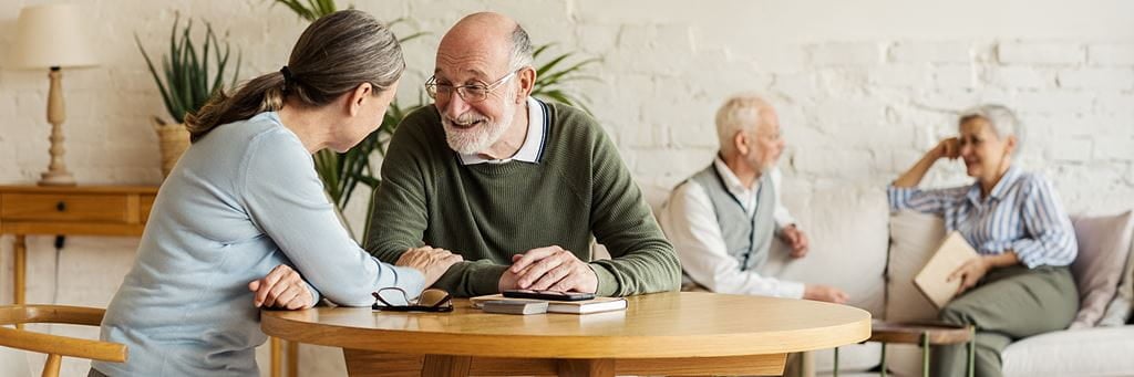 A senior couple laughs together while another couple relaxes in the background.