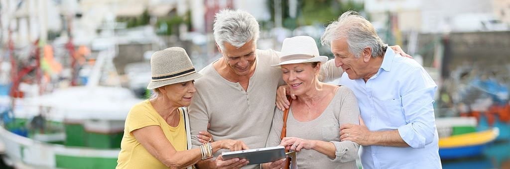 Four seniors look at a tablet while traveling in retirement.
