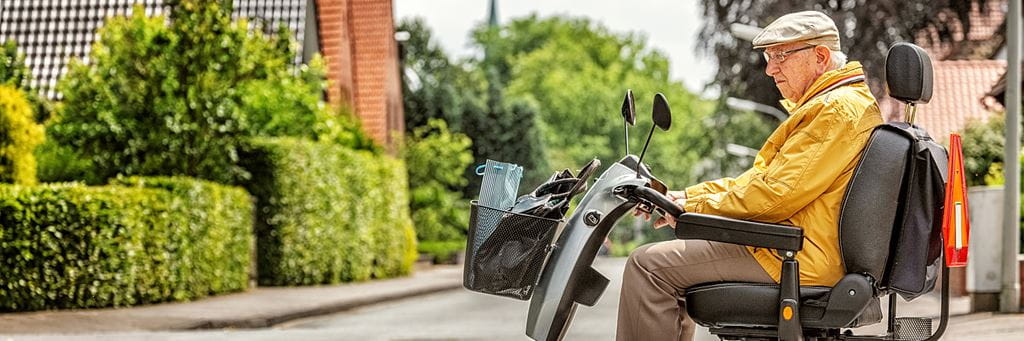 A senior man uses a mobility scooter outside.