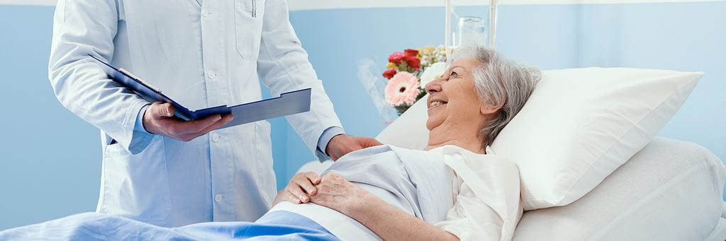 A senior woman in a hospital bed speaking with her doctor.