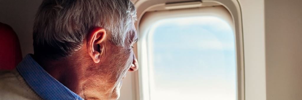 An older man stares out the window of an airplane.