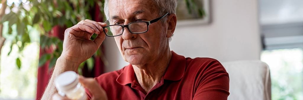 Older man in glasses reads a prescription bottle label.