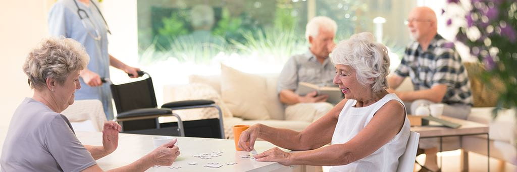 Seniors play games and talk in a sunny assisted living facility.