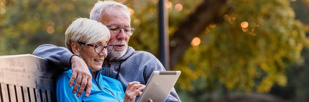 An elderly couple reviews a nondurable power of attorney on a tablet while sitting on a bench.