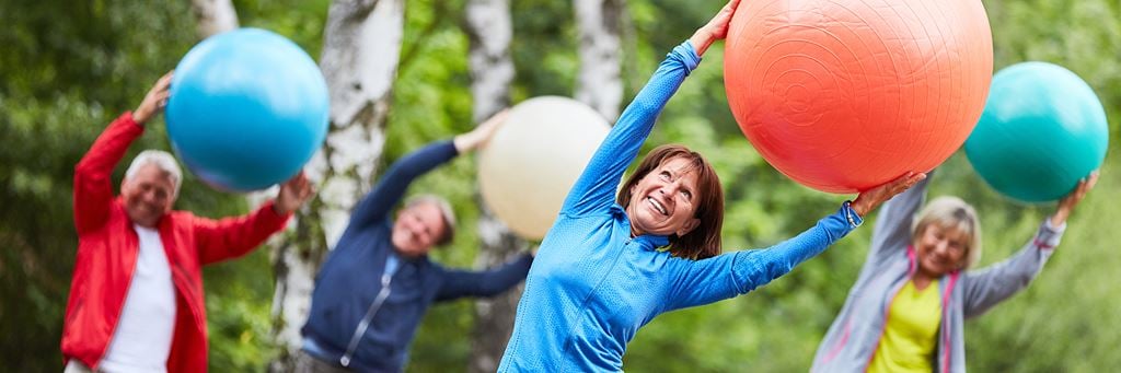 A group of happy, retired seniors attends an exercise class outside.