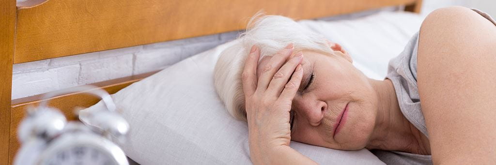 An elderly person holding their head with one hand while laying in bed.