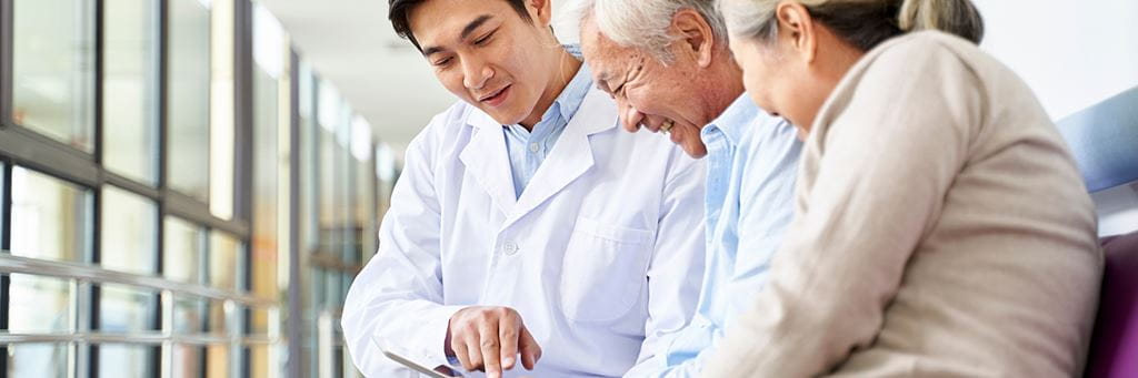 A doctor refers to a tablet to show a senior patient health insurance details.